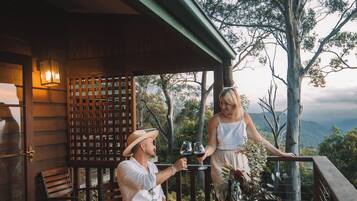 A wooden deck with a table and chairs, overlooking a scenic landscape with trees and mountains.