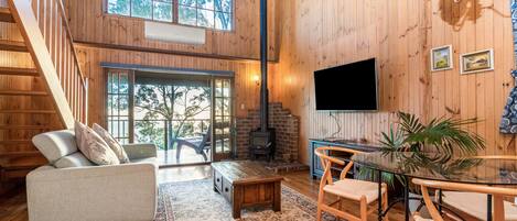 A wooden interior with a sofa, a dining table, chairs, a staircase, and a fireplace.