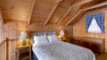 Une chambre à coucher dans une cabane en bois, avec un lit, des tables de chevet, une commode et une fenêtre ornée de rideaux à motifs.