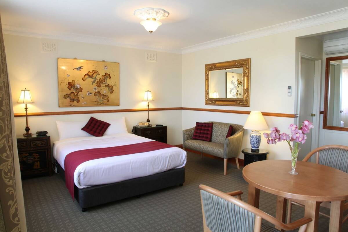 A hotel room with a bed, bedside tables, a sofa, a round table, and a mirror.