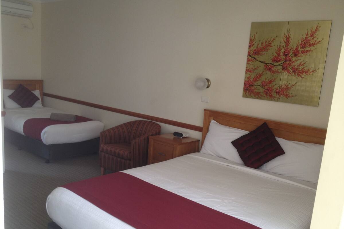 A hotel room with two beds, a wooden headboard, a nightstand, a chair, and a painting on the wall.