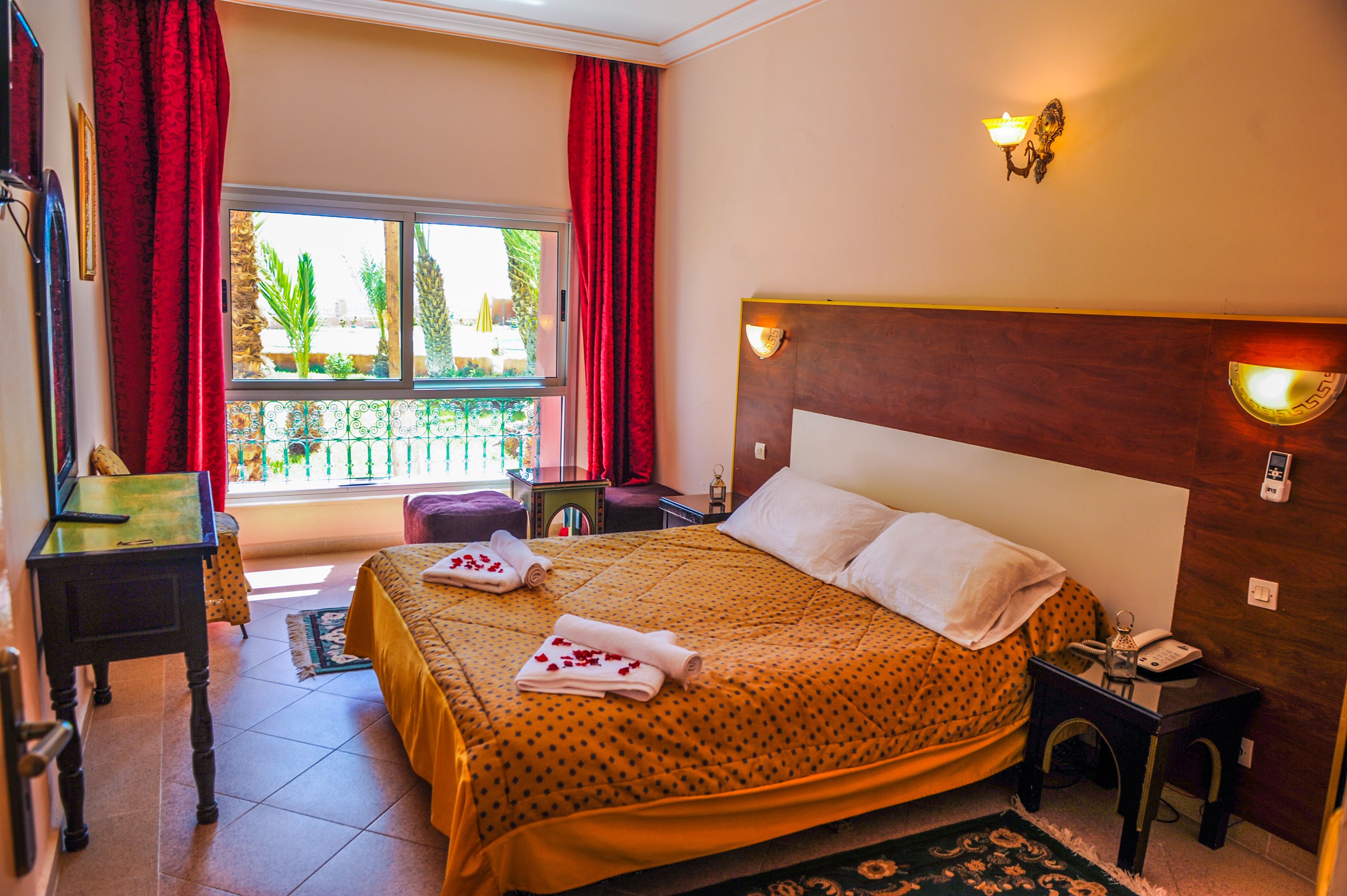 Habitación de hotel con cama, escritorio, silla y ventana con cortinas rojas, y vista al exterior.