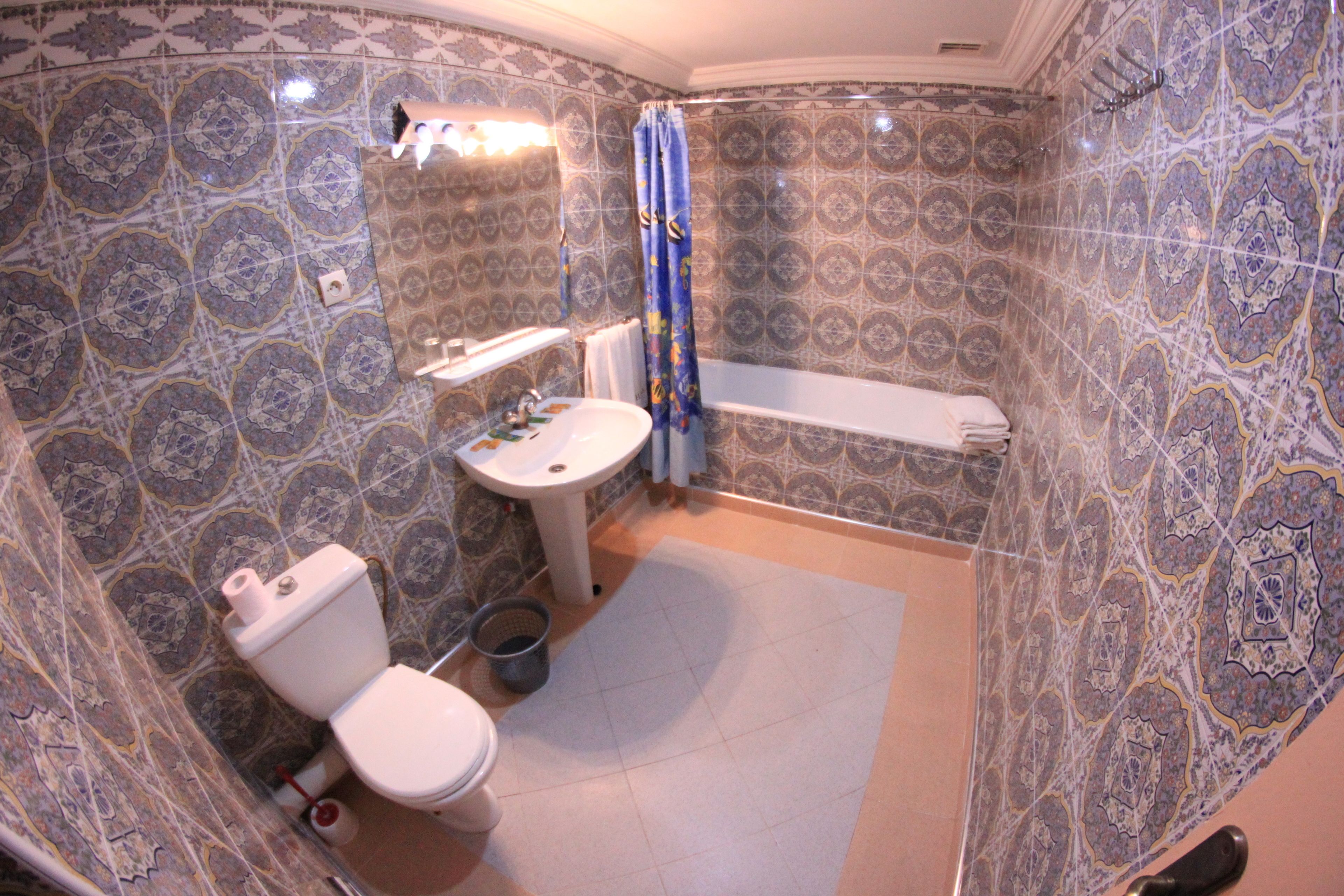 Une salle de bain avec des carreaux décorés, des toilettes, un lavabo et une baignoire.
