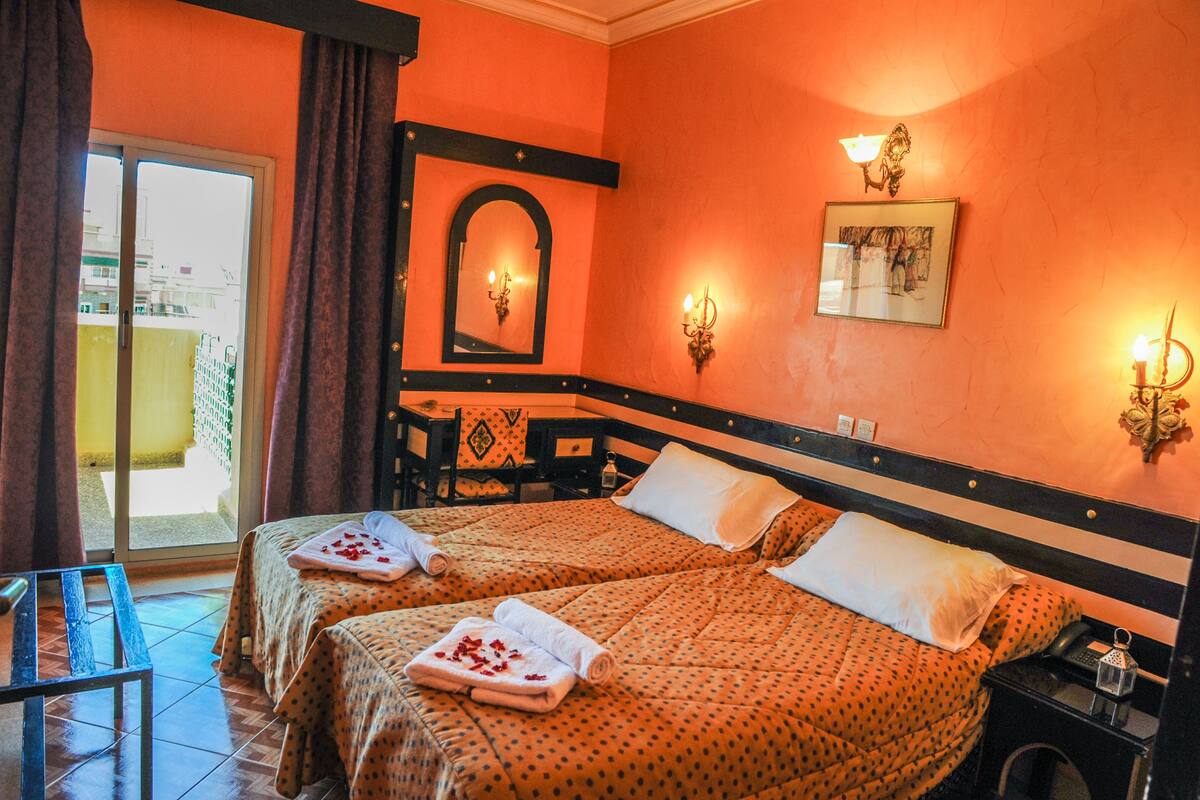 A hotel room with two beds, a balcony, a small table, and a chair.
