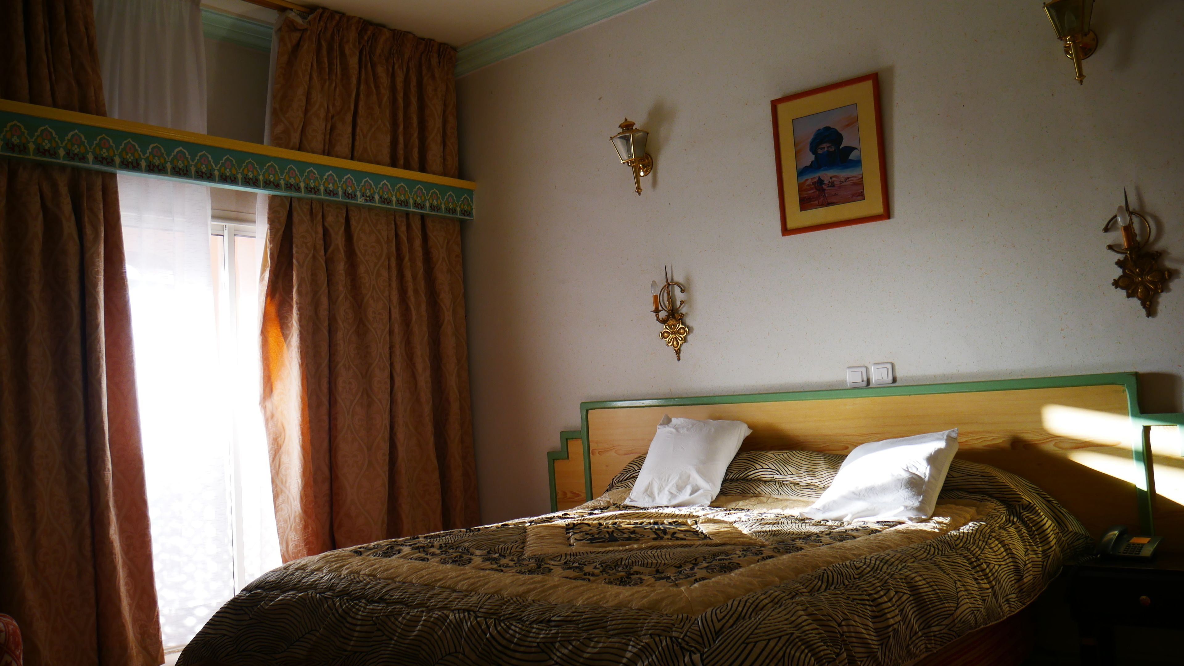 A bedroom with a bed, curtains, a wall-mounted lamp, and a framed picture.