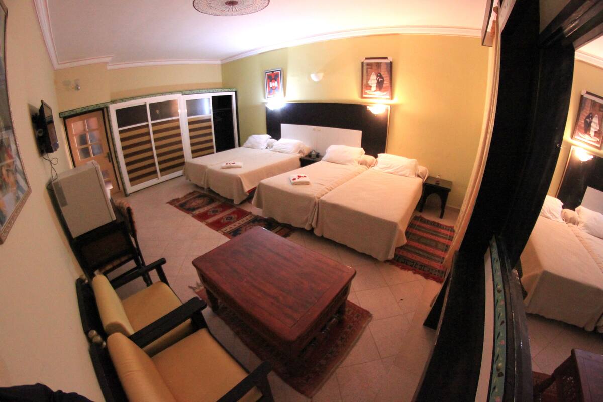 A hotel room with two beds, a wooden coffee table, a sofa, a TV, and a wardrobe.