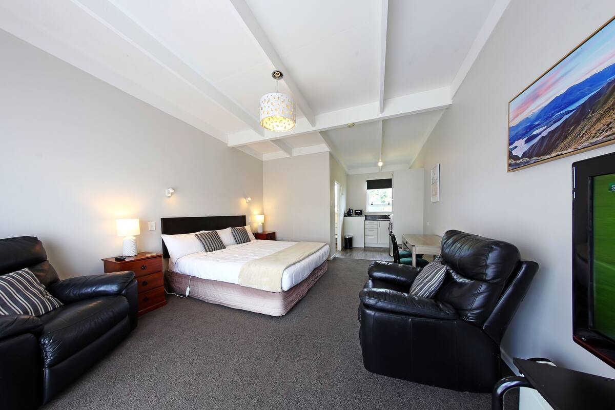 A modern hotel room with a large bed, a leather sofa, a desk, and a TV.