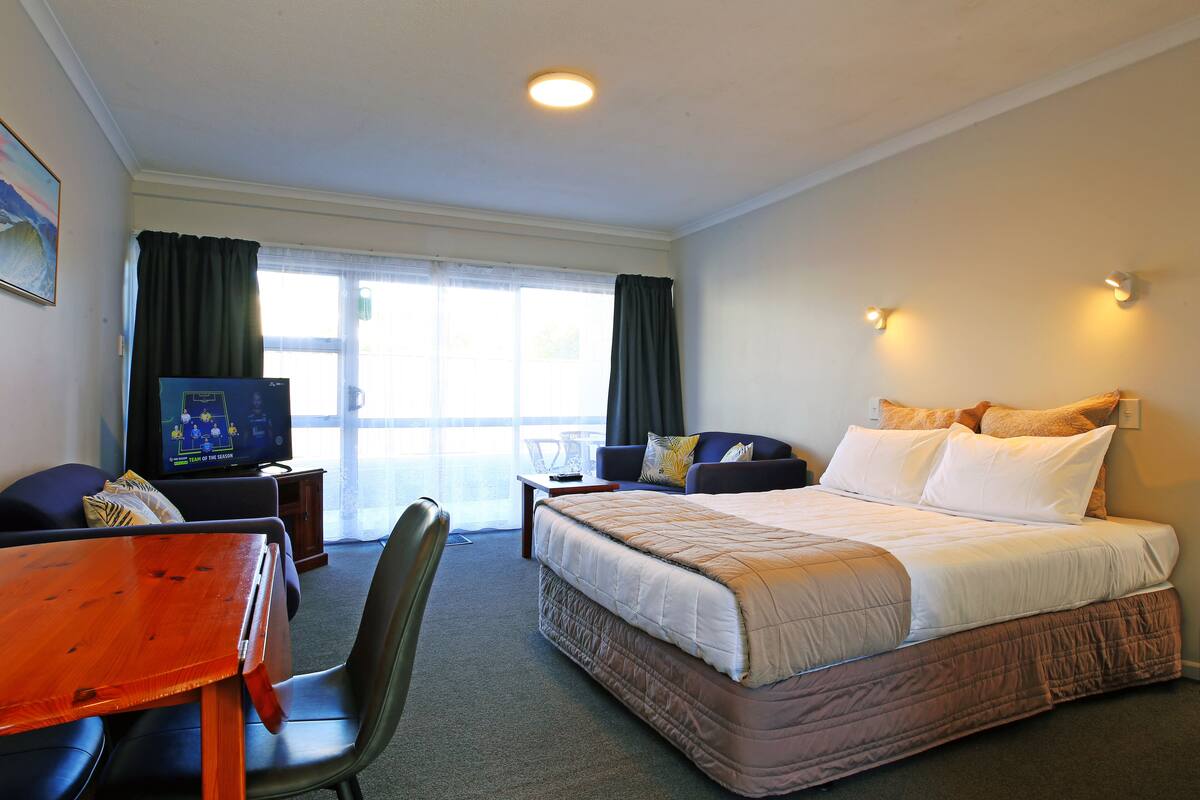 A hotel room with a bed, a desk, a chair, a television, and a window with curtains.
