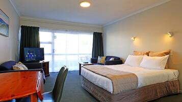 Una habitación de hotel con cama, escritorio, silla, televisor y ventana con cortinas.