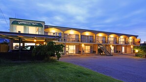 Ein Motel mit zweistöckiger Bauweise, einem überdachten Parkplatz und einer Treppe, die zum oberen Stockwerk führt.