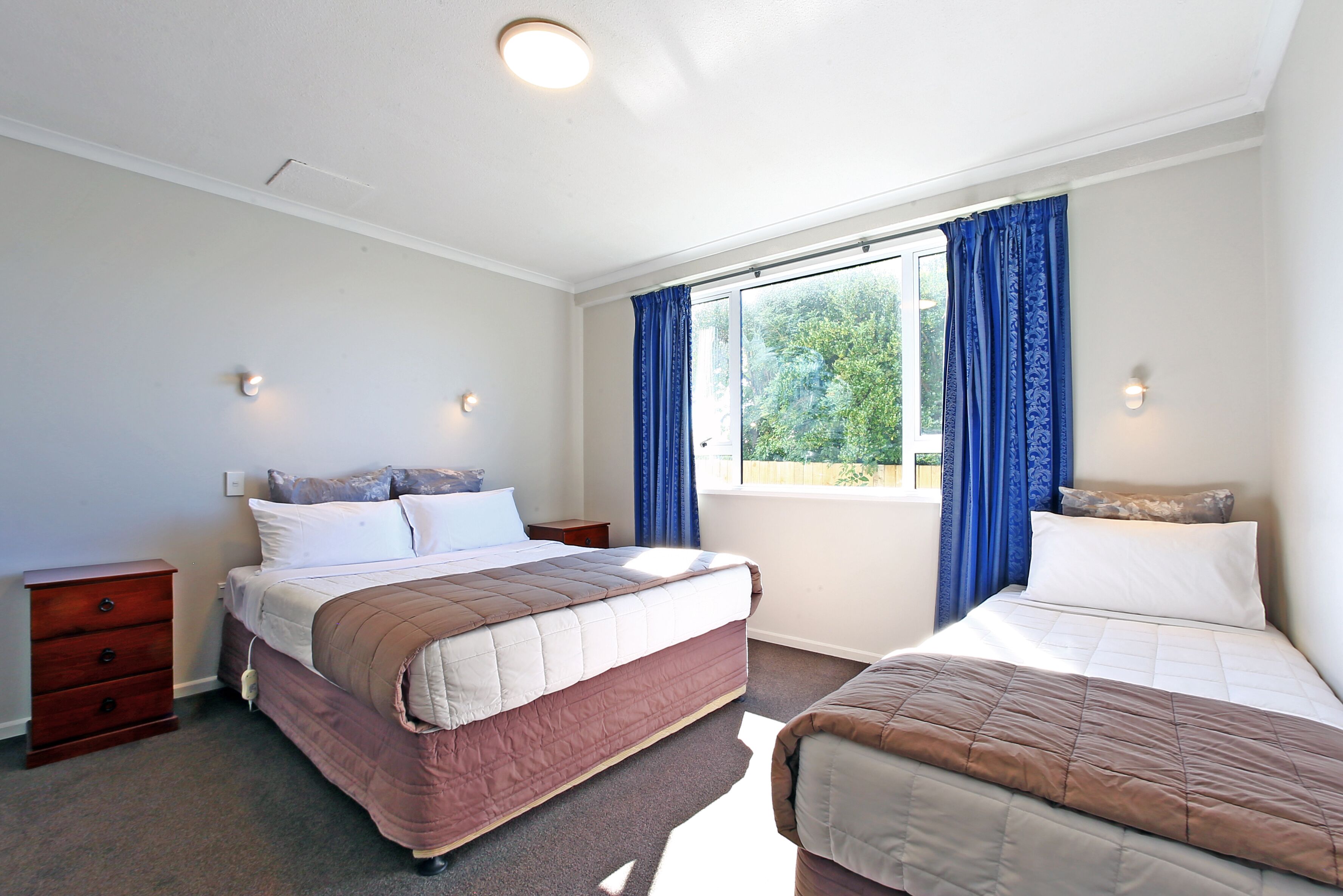 A bedroom with two beds, a nightstand, a dresser, and a window with curtains.