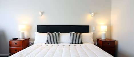 A neatly made bed with a white quilt, two striped pillows, and a black headboard. There are two bedside tables with lamps and a remote control on one.