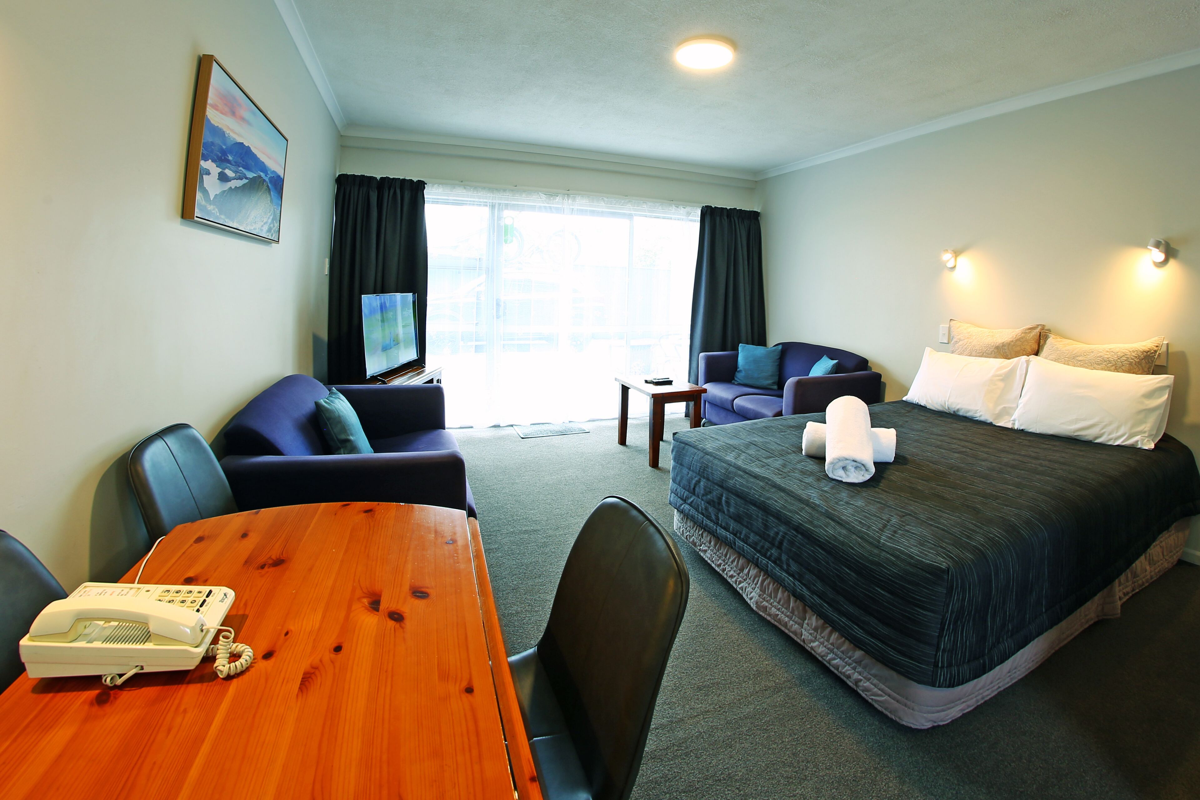 A hotel room with a bed, a desk with a telephone, a chair, a sofa, and a television.