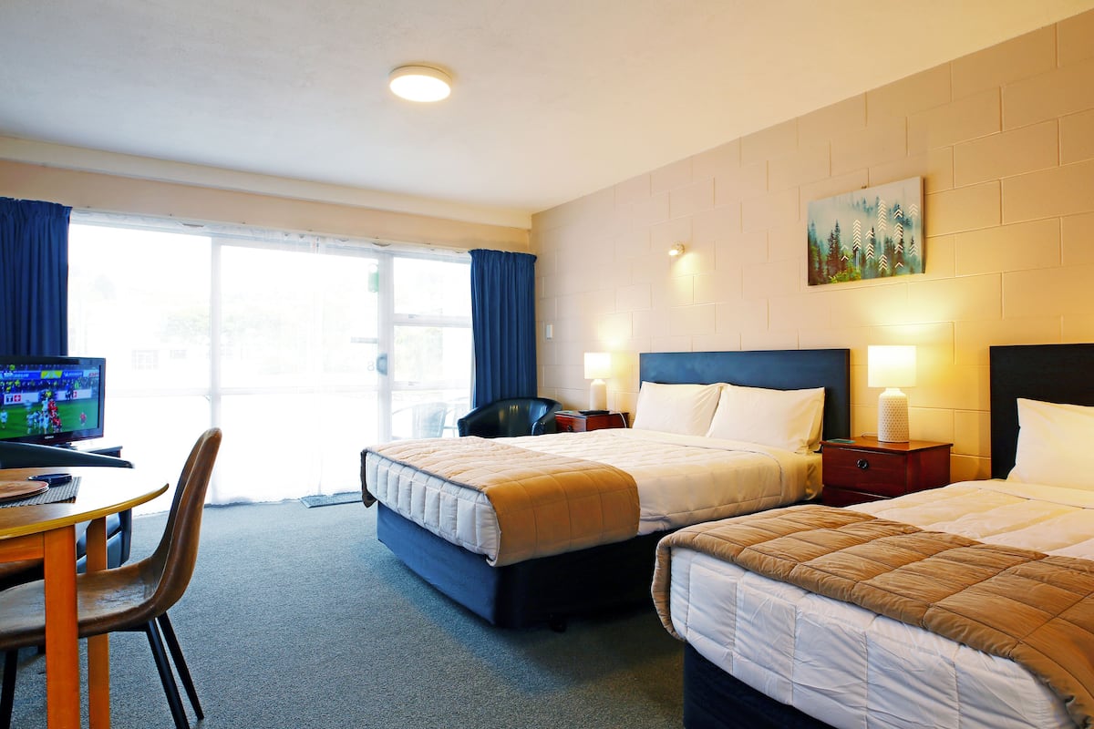 A hotel room with two beds, a desk with a computer, and a window with curtains.