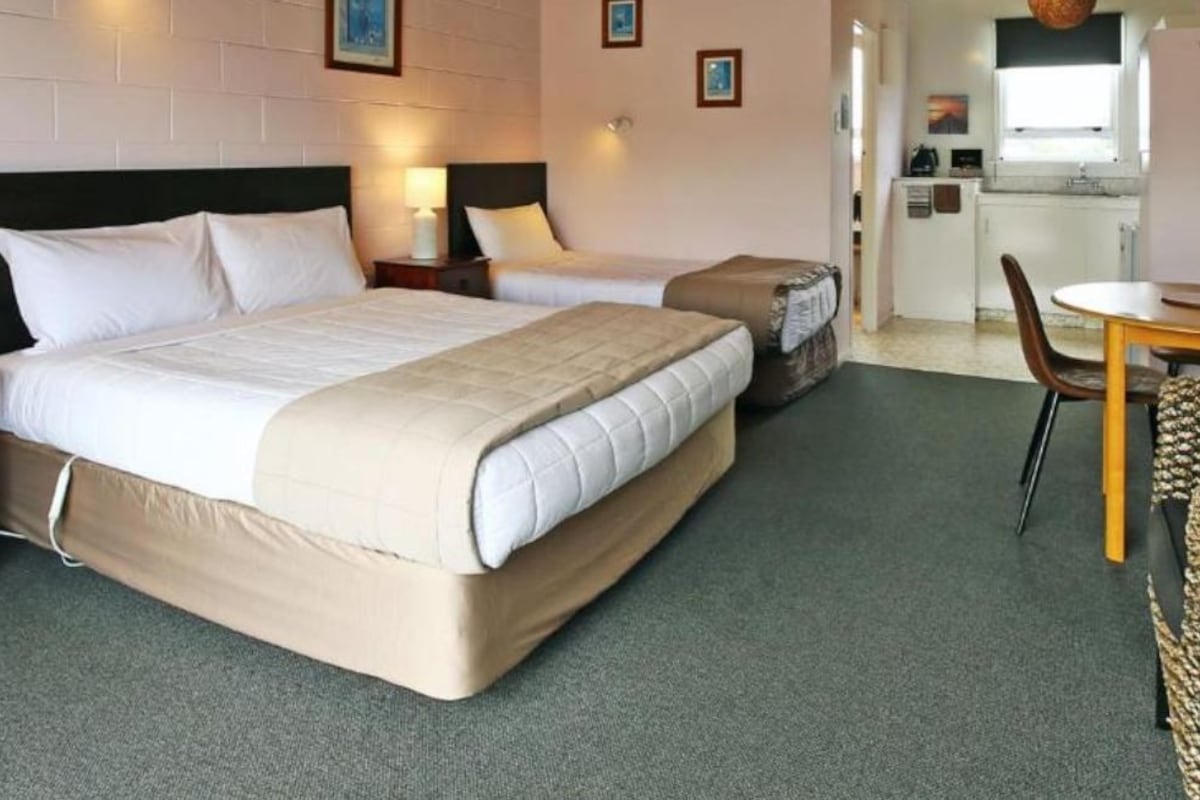 A hotel room with two beds, a desk, and a kitchenette.