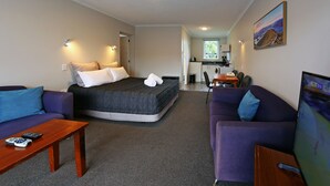 Ein Hotelzimmer mit einem Bett, einem violetten Sofa, einem Holztisch, einem Fernseher und einem Gemälde an der Wand.