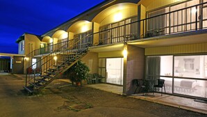 Ein Hotel mit zweistöckiger Struktur, einer Treppe, die zu einer oberen Ebene führt, und einem Sitzbereich im Freien mit Stühlen und Tischen.