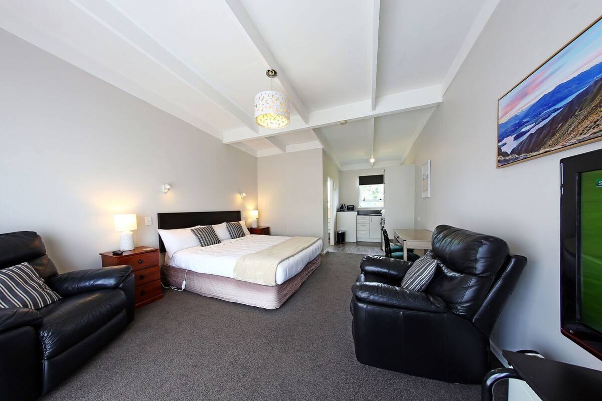 A bedroom with a bed, two black leather sofas, a desk, and a TV.