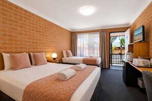 A hotel room with two beds, a desk, a chair, a lamp, and a view of the outdoors.