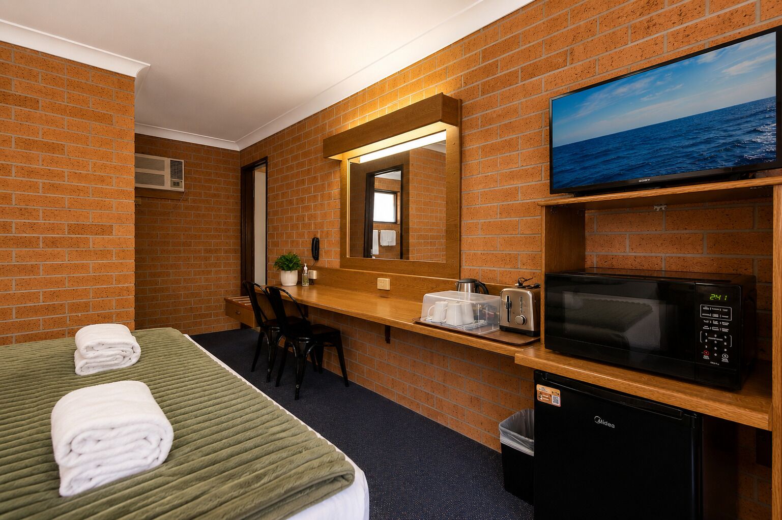 A hotel room with a bed, a desk, a microwave, a television, and a trash bin.