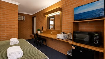 Habitación de hotel con cama, escritorio, microondas, televisión y cubo de basura.