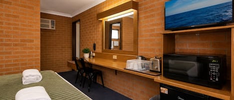 Habitación de hotel con cama, escritorio, microondas, televisión y cubo de basura.