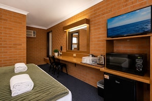 Habitación de hotel con cama, escritorio, microondas, televisión y cubo de basura.