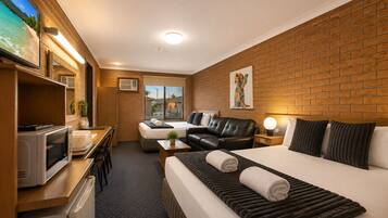 A hotel room with a bed, a desk with a microwave, a TV, and a window with a view of buildings.