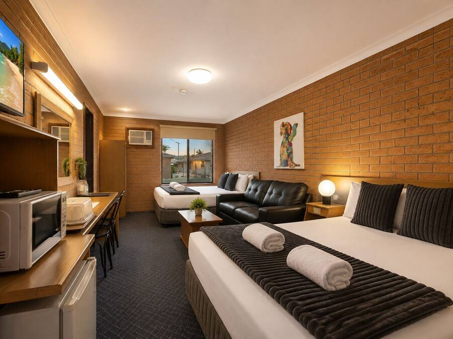 Habitación de hotel con cama, escritorio con microondas, televisión y ventana con vista a edificios.