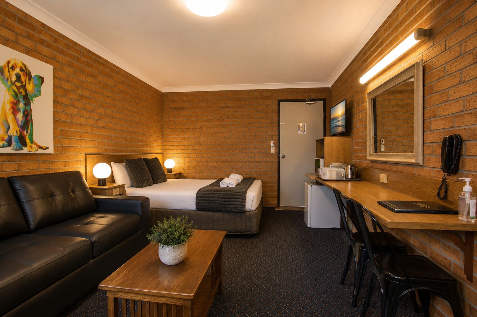 A hotel room with a bed, a desk, a small kitchenette, a seating area, and a painting on the wall.