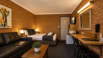 A hotel room with a bed, a desk, a small kitchenette, a seating area, and a painting on the wall.