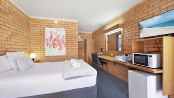 Una habitación de hotel con cama, escritorio, microondas y refrigerador.