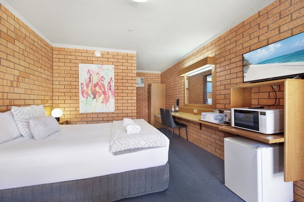 Una habitación de hotel con cama, escritorio, microondas y refrigerador.
