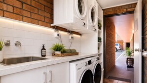 A laundry area with two front-loading washing machines, a sink, and a countertop with a plant and a bottle. - Royal Palms Motor Inn (Coffs Harbour)