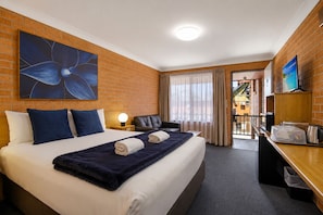 Habitación de hotel con cama, escritorio, silla, televisor y ventana grande.