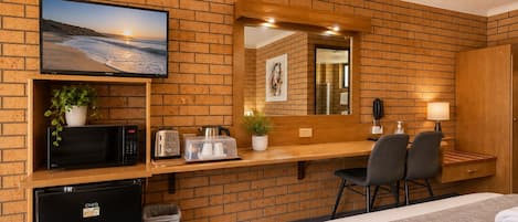 Habitación de hotel con pared de ladrillo, televisor, microondas, tostadora, refrigerador pequeño, escritorio con sillas y cama con toallas.
