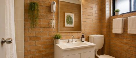 A bathroom with a brick wall, a white sink, a toilet, and a window with a towel rack.