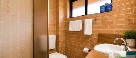 Baño con ducha, inodoro, lavabo y ventana, con toallas.