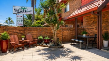 A Royal Palms Motor Inn with a patio area featuring wooden chairs, tables, and potted plants.
