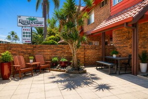 Un Motor Inn Royal Palms con un área de patio que cuenta con sillas, mesas y plantas en macetas.