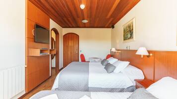 A hotel room with two beds, wooden ceiling, a TV, a painting, and a red chair.