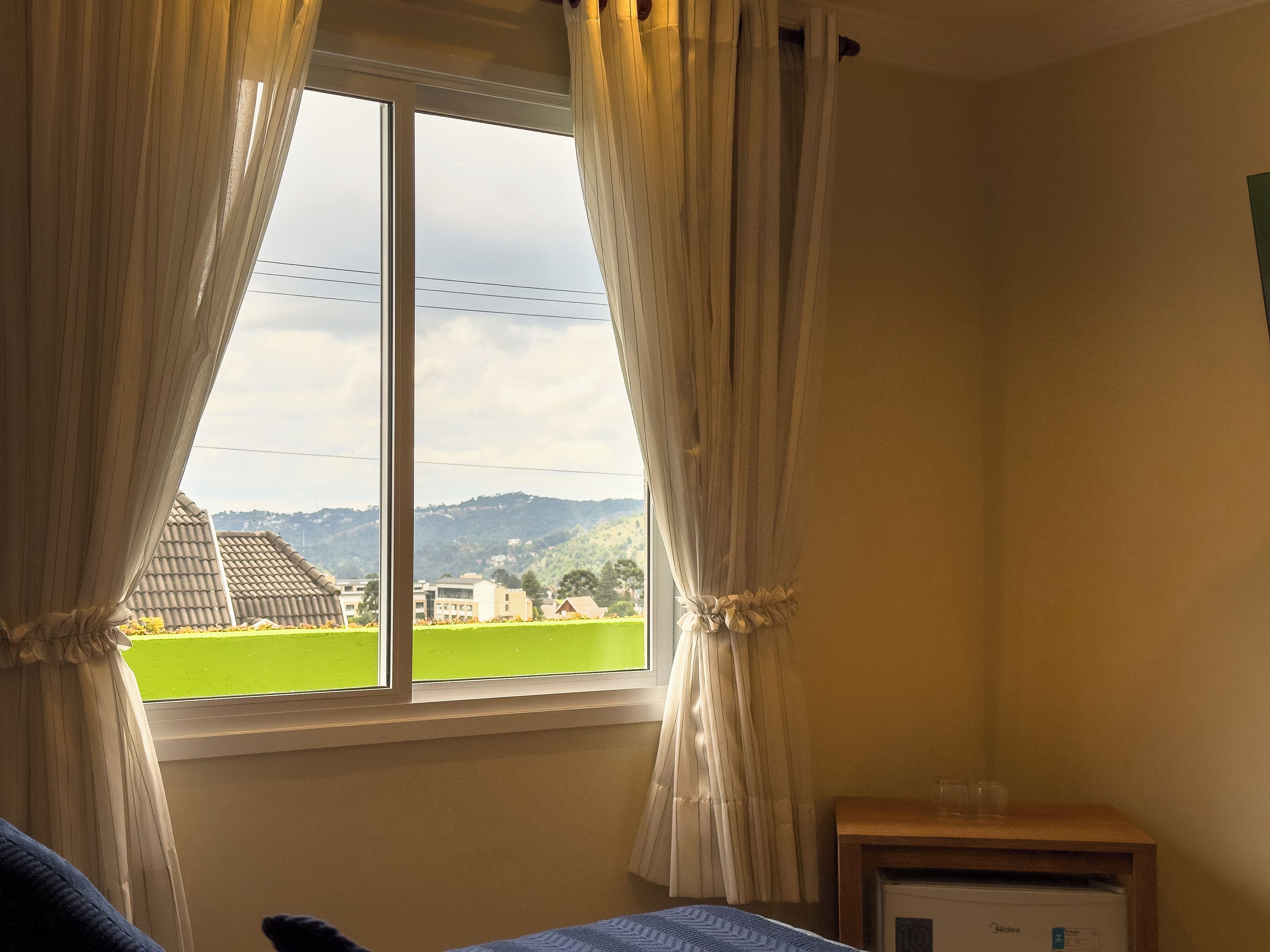 Una habitación con una cama, una mesita con vasos y una ventana con cortinas.