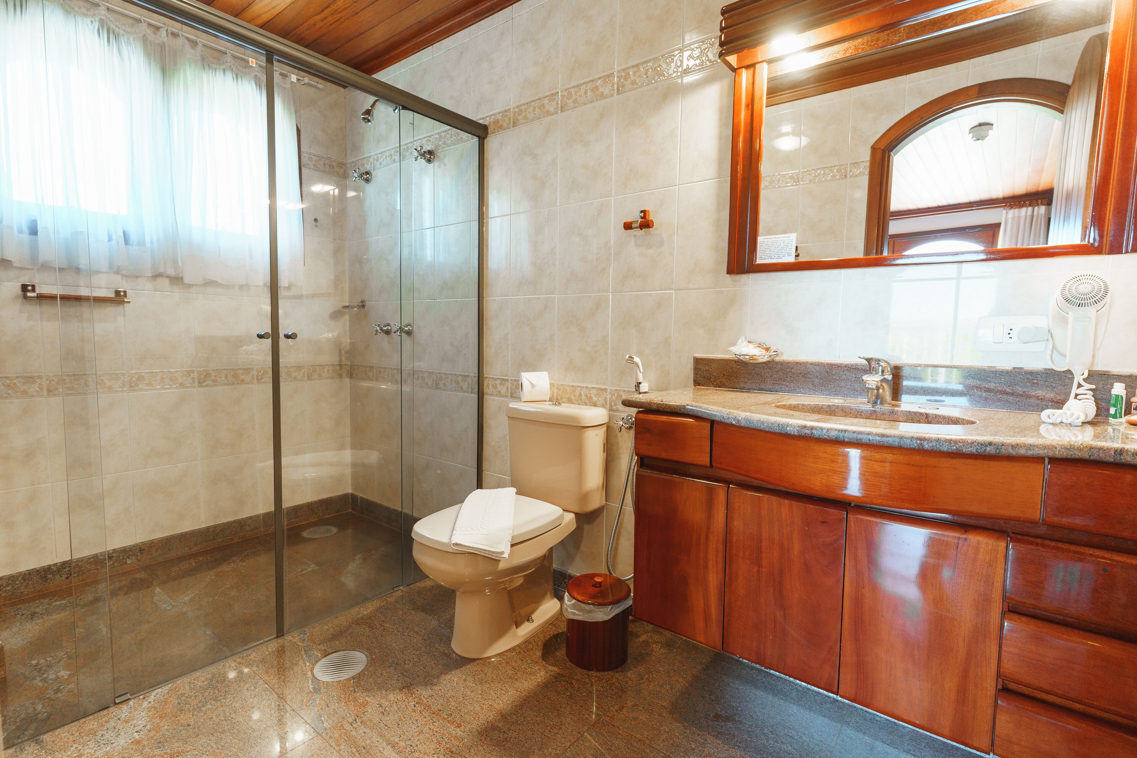 A bathroom with a glass shower enclosure, a toilet, a sink with a mirror, and wooden cabinets.