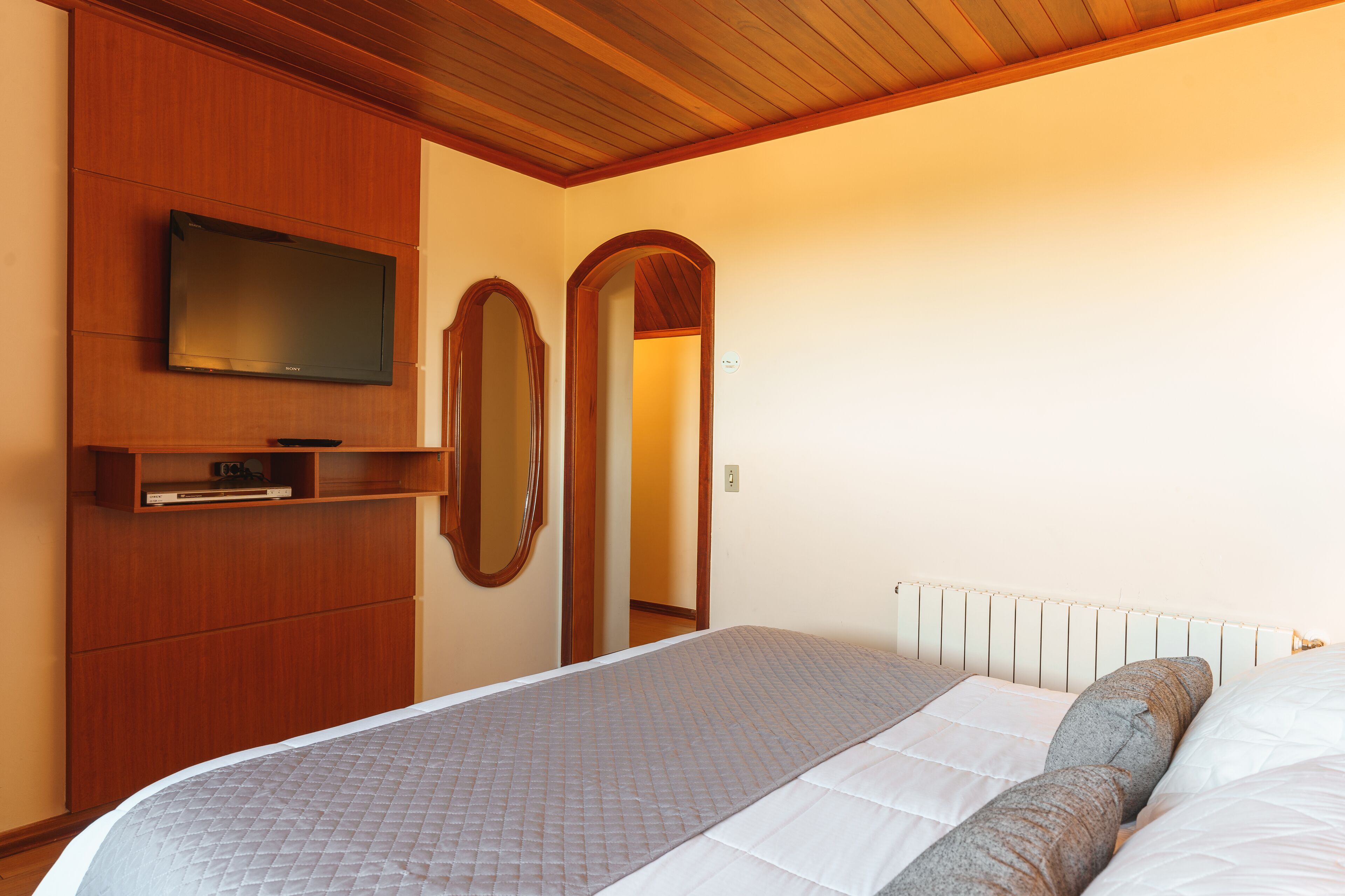 A bedroom with a bed, a TV mounted on a wooden cabinet, and a mirror.