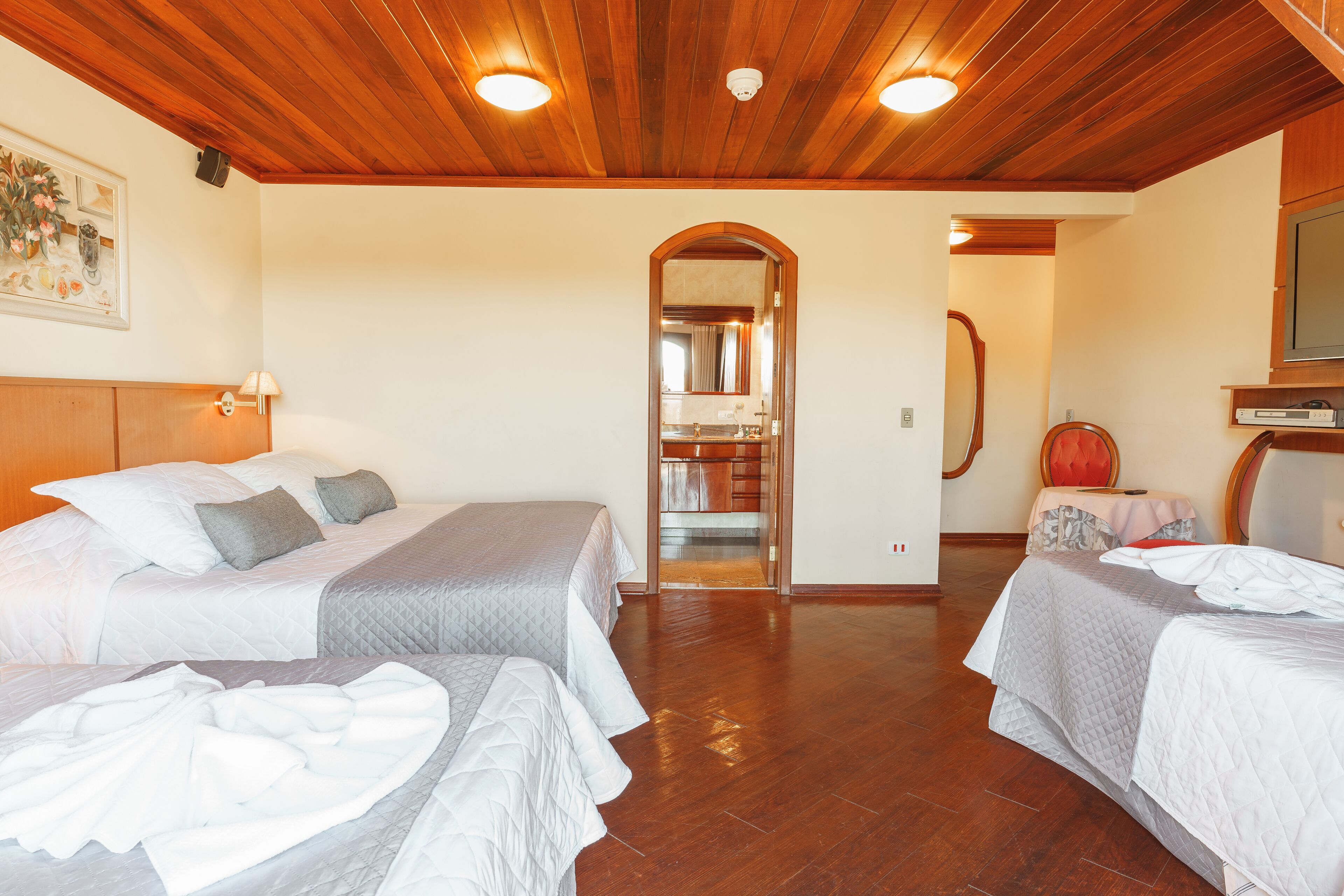 Habitación de hotel con dos camas, techo de madera y un pasillo que conduce a un baño.
