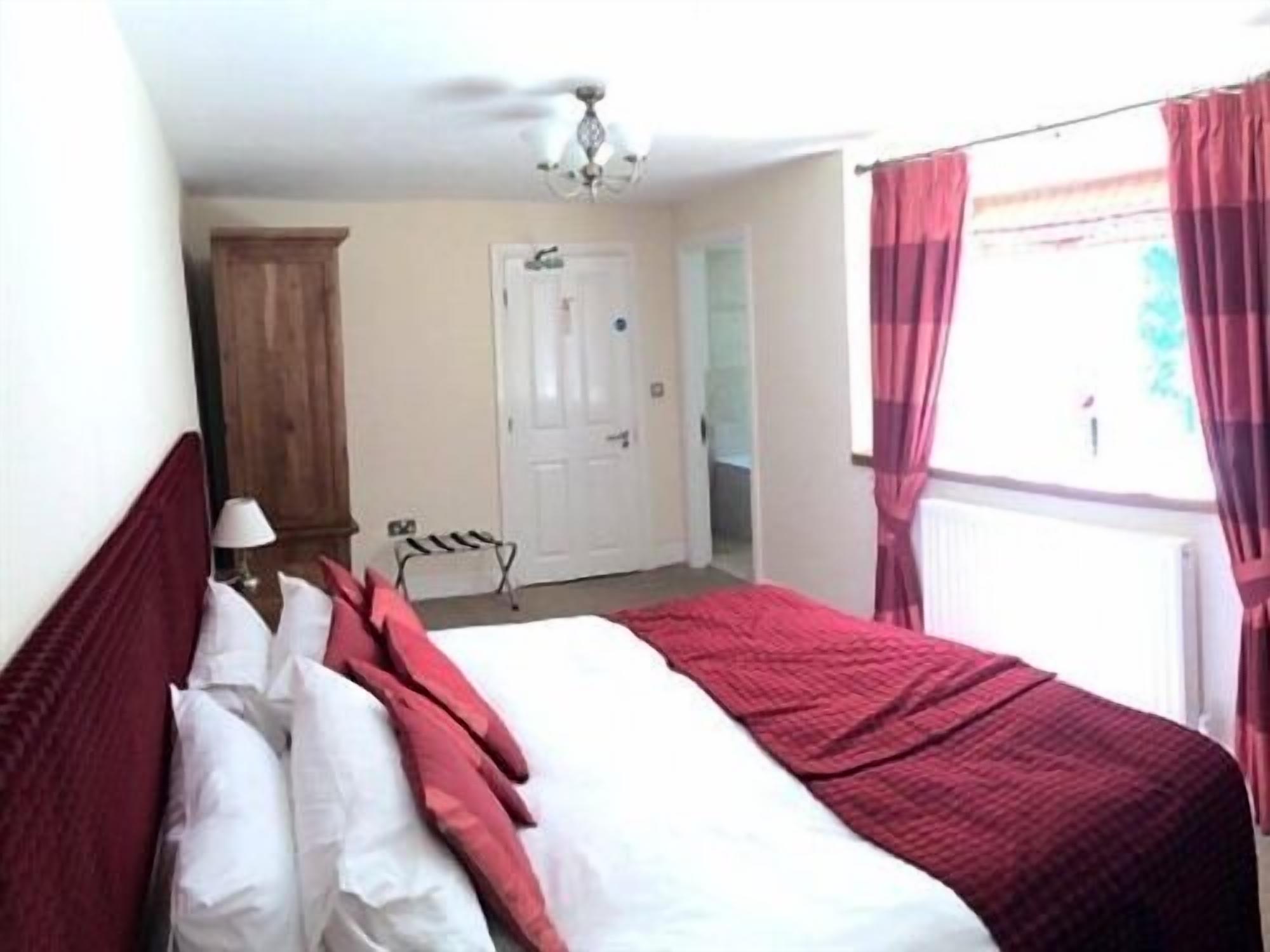 Un dormitorio con cama, mesita de noche, lámpara, puerta y ventana con cortinas.