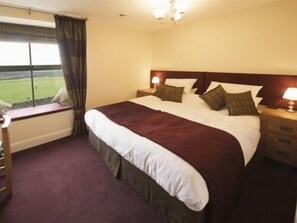 A hotel room with a large bed, a window with curtains, a bedside table with a lamp, and a view of the outdoors.