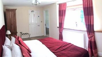 A bedroom with a bed, a wooden wardrobe, a ceiling fan, and a window with curtains.
