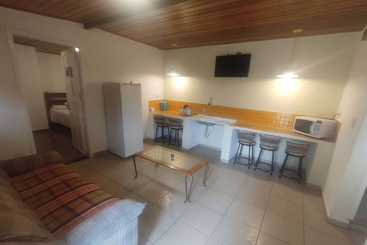 Un espacio habitable compacto con kitchenette, un sofá y un televisor montado en la pared.