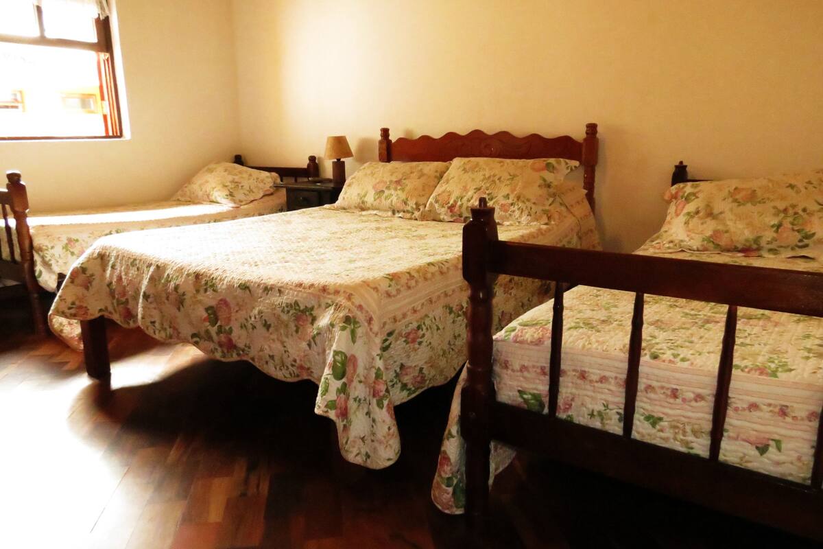 Una habitación con dos camas de madera con ropa de cama estampada, una mesita de noche de madera con una lámpara, y una ventana que deja entrar luz natural.